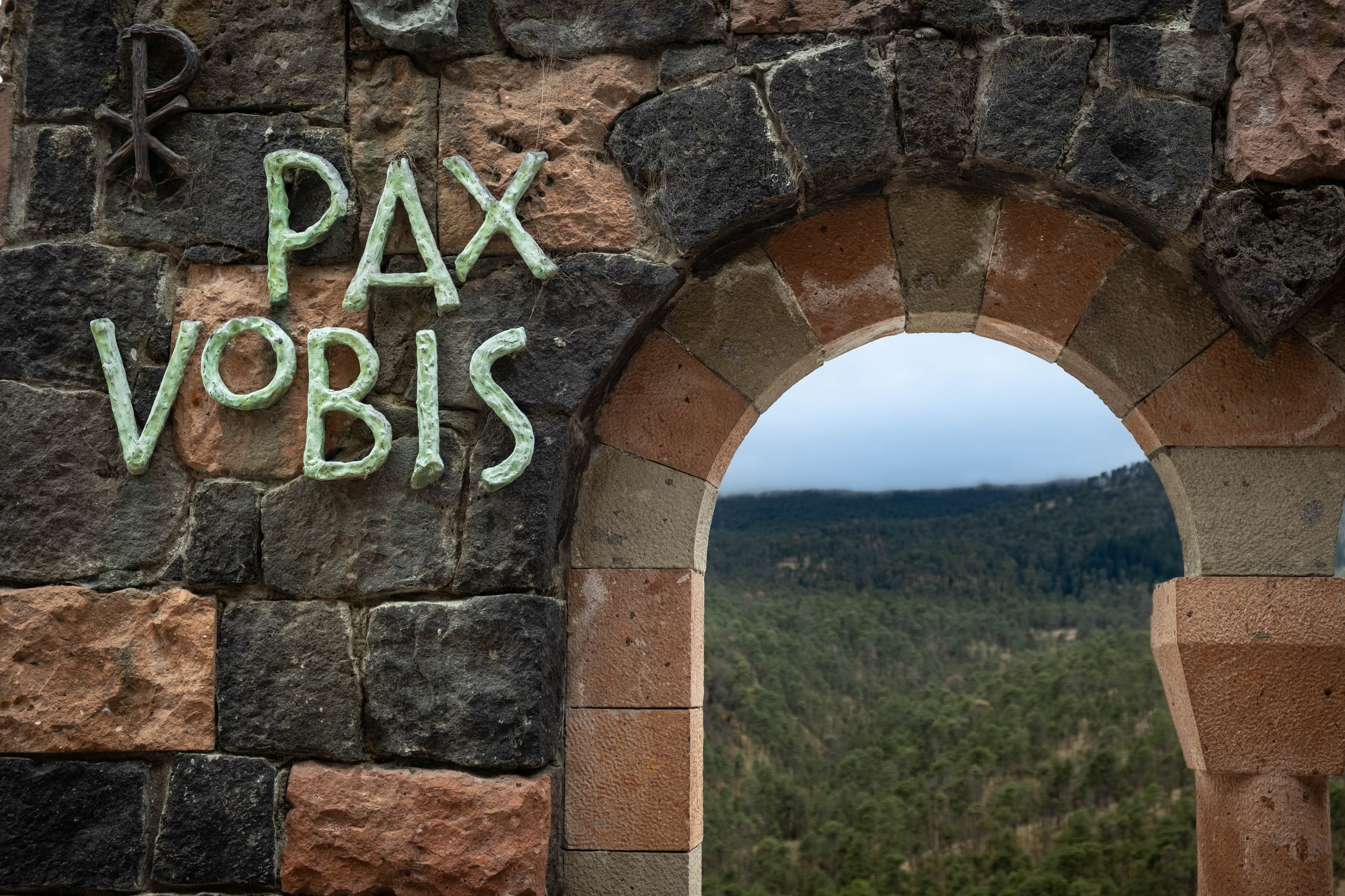 Letras Pax vobis junto a un arco abierto al bosque